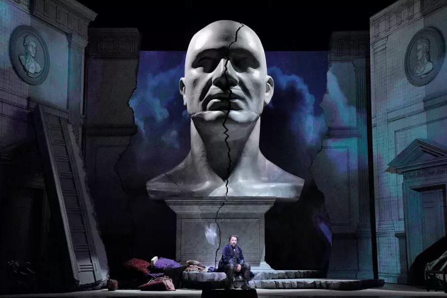 A giant bust of a man looms over two actors on stage in a production of Don Giovanni 在贝博体彩app.
