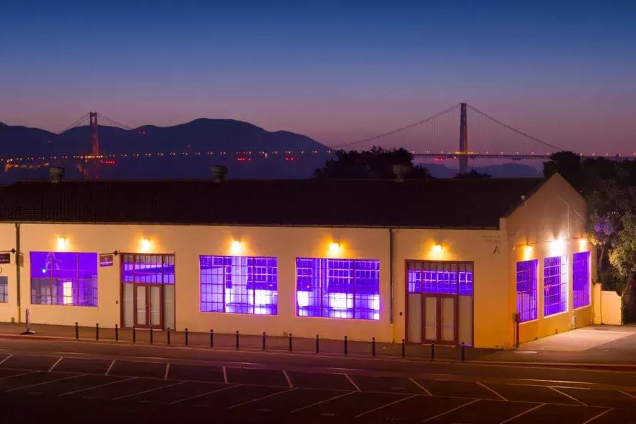 The Fort Mason building is lit with a purple interior light at night, 以桥为背景.