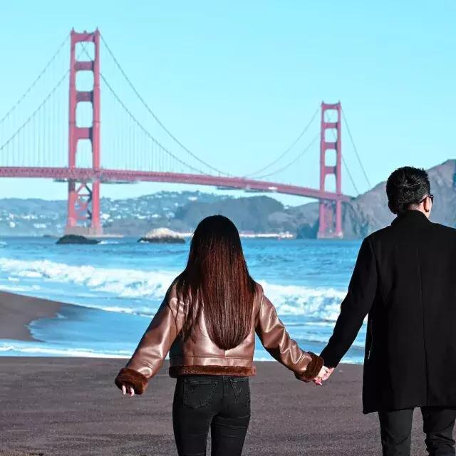 一对情侣在贝克海滩牵手，背景是金门大桥 